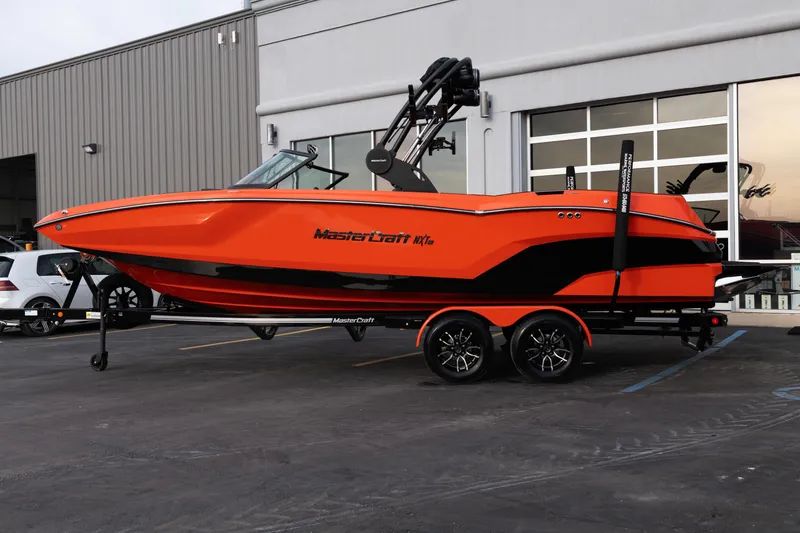 Slide: The Image of 2026 MasterCraft NXT24 boat in vibrant orange on a trailer outside a building. - 3