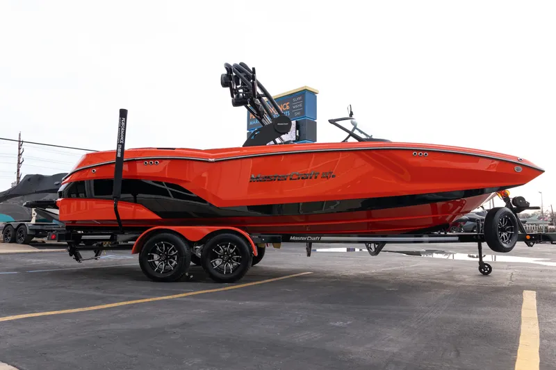 Slide: The Image of 2026 MasterCraft NXT24 boat in vibrant orange on a trailer, parked outdoors. - 39
