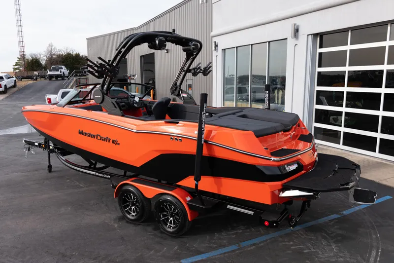 Slide: The Image of 2026 MasterCraft NXT24 boat in vibrant orange, parked outside a modern building. - 4