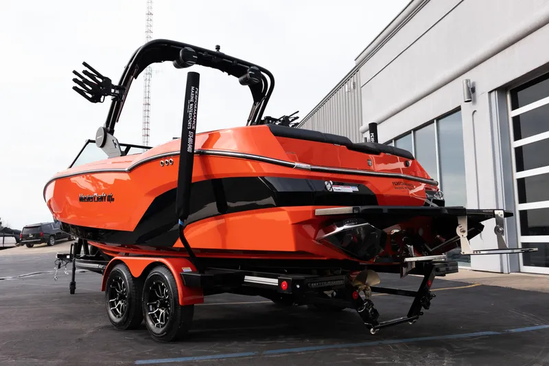 Slide: The Image of 2026 MasterCraft NXT24 boat in vibrant orange, parked on a trailer near a building. - 5
