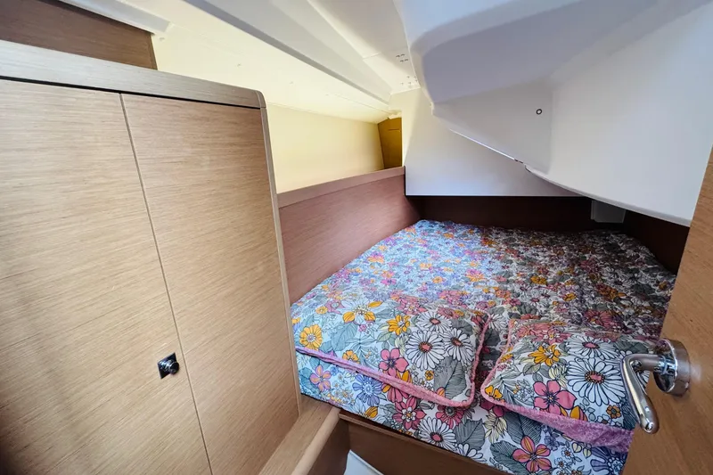 Slide: The Image of 2024 Jeanneau Sun Odyssey 349 interior with wooden cabinet and floral-patterned bedding. - 52
