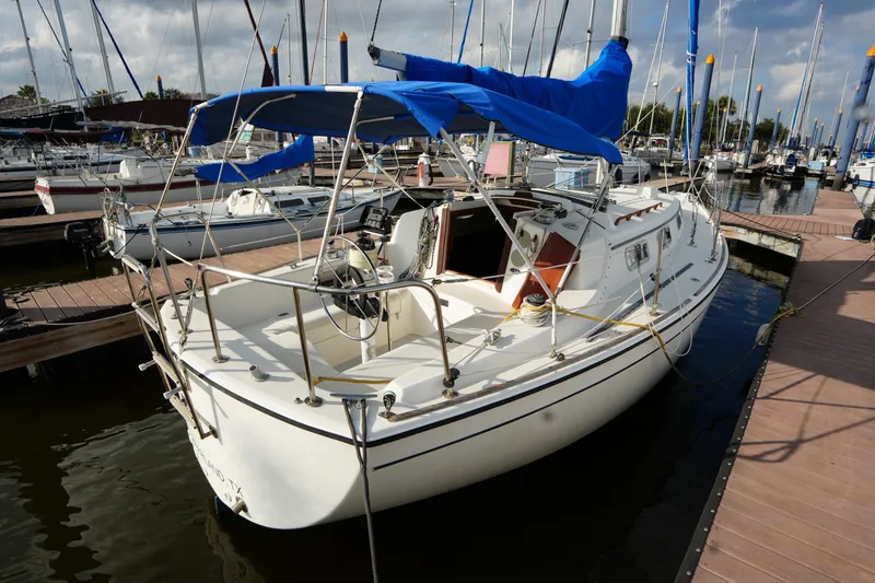 Slide: The Image of 1985 Pearson 303 sailboat docked at marina, featuring blue canopy and white hull. - 4