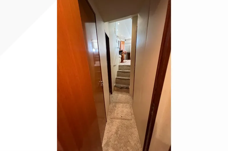 Slide: The Image of Narrow hallway inside 1999 Viking 60 CPMY yacht, featuring carpeted stairs and wooden doors. - 76