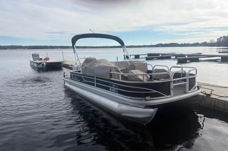 The Image of 2019 Sun Tracker Fishin' Barge 20 DLX pontoon boat docked on a calm lake. - 0