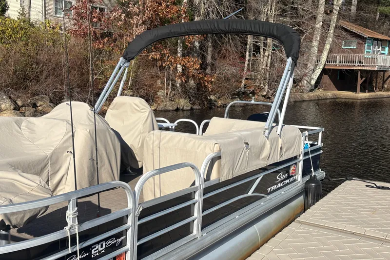 Slide: The Image of 2019 Sun Tracker Fishin' Barge 20 DLX pontoon boat docked by a lakeside cabin. - 2