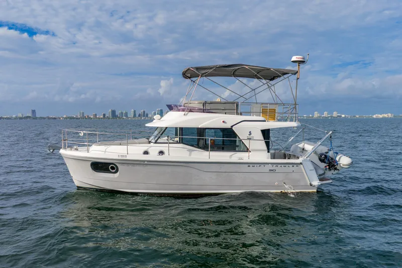 Slide: The Image of 2017 Beneteau Swift Trawler 30 on water with city skyline in background. - 5