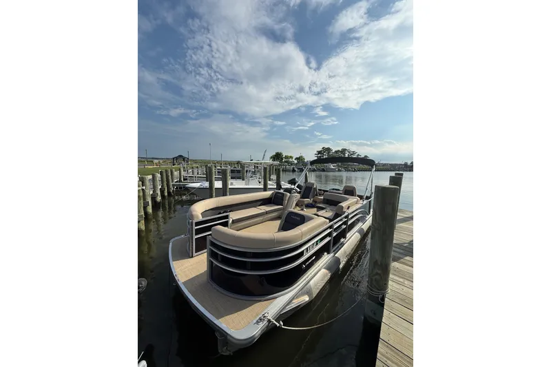 The Image of 2025 Harris Cruiser 230 pontoon boat docked under a partly cloudy sky. - 1