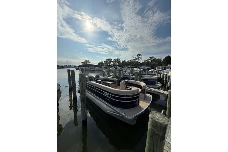 Slide: The Image of 2025 Harris Cruiser 230 pontoon boat docked under a partly cloudy sky. - 3