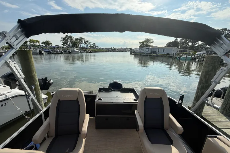 Slide: The Image of 2025 Harris Cruiser 230 pontoon boat docked, featuring comfortable seating and scenic waterfront view. - 6