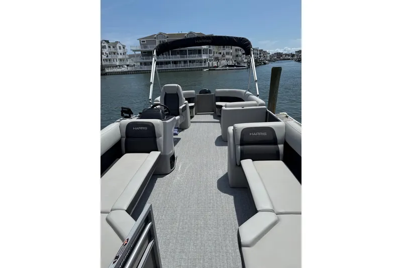 Slide: The Image of 2025 Harris Cruiser 230 pontoon boat with spacious seating on a sunny waterfront. - 2