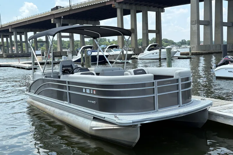 The Image of 2025 Harris Cruiser 230 pontoon boat docked near a bridge on a sunny day. - 0