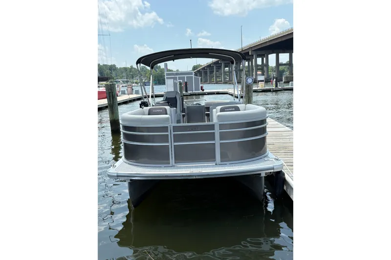 Slide: The Image of 2025 Harris Cruiser 230 pontoon boat docked at marina under clear sky. - 2
