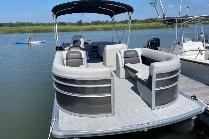 Slide: The Image of 2025 Harris Cruiser 230 pontoon boat docked on a calm lake with kayaker nearby. - 3
