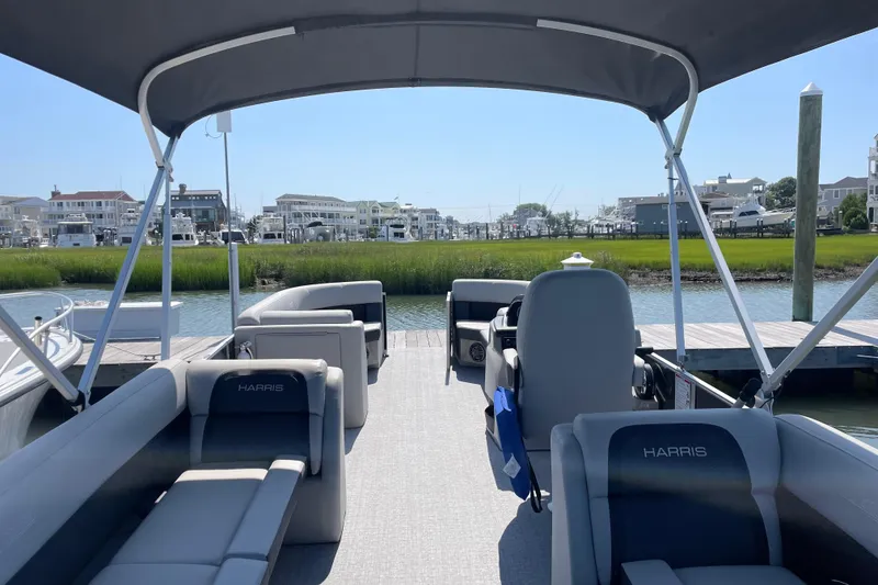 Slide: The Image of 2025 Harris Cruiser 230 pontoon boat interior with seating, docked by waterfront homes. - 5