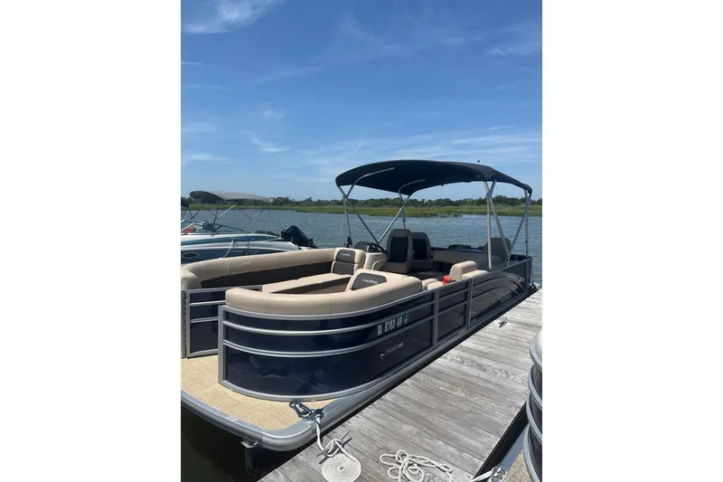 Slide: The Image of 2025 Harris Cruiser 230 pontoon boat docked on a sunny day by the lake. - 2