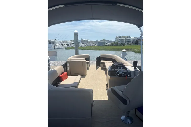 Slide: The Image of 2025 Harris Cruiser 230 pontoon boat interior with steering wheel, docked by waterfront homes. - 6