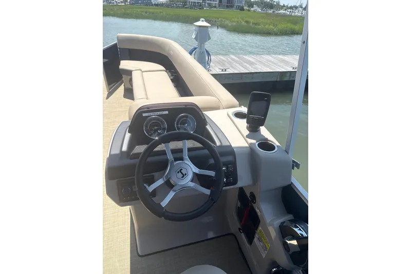 Slide: The Image of 2025 Harris Cruiser 230 boat interior with steering wheel and dashboard, docked by the water. - 7