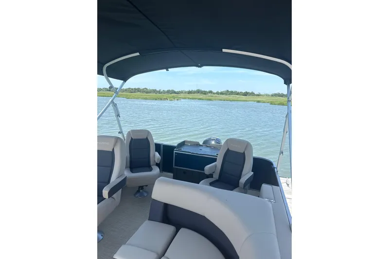 Slide: The Image of 2025 Harris Cruiser 230 boat interior with seating, overlooking serene water and greenery. - 9