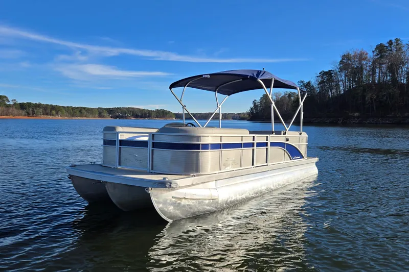 Slide: The Image of 2023 Bennington 22 SSR pontoon boat on a serene lake under clear blue skies. - 1