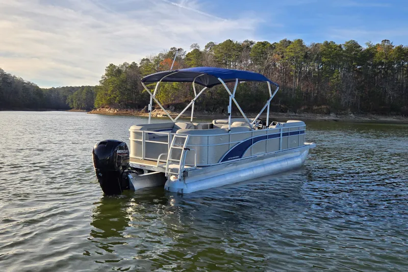 Slide: The Image of 2023 Bennington 22 SSR pontoon boat on a serene lake with forested shoreline. - 2