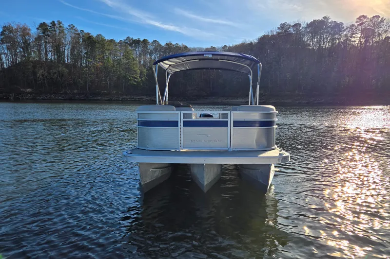 Slide: The Image of 2023 Bennington 22 SSR pontoon boat on a serene lake with forested shoreline. - 6