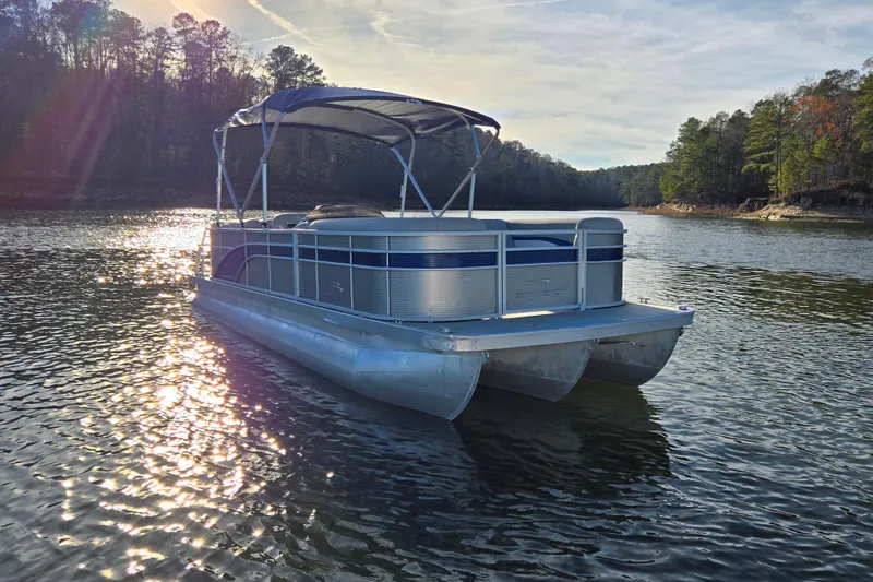 Slide: The Image of 2023 Bennington 22 SSR pontoon boat on a serene lake with sunlit water. - 7