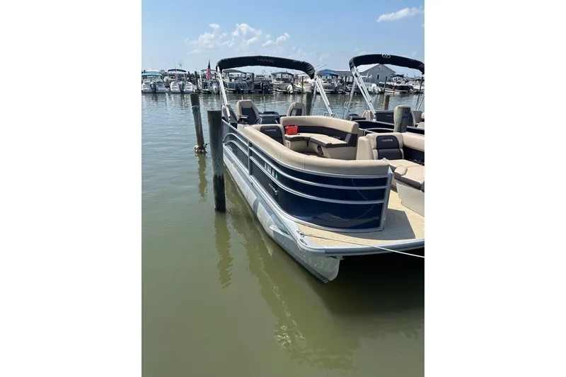 Slide: The Image of 2025 Harris Cruiser 230 pontoon boat docked at a marina under a clear sky. - 3