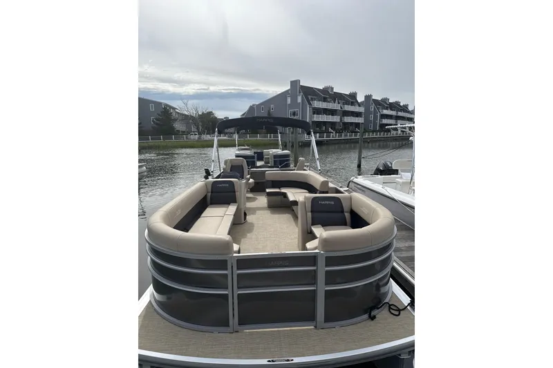 Slide: The Image of 2025 Harris Cruiser 230 pontoon boat docked by waterfront homes. - 2