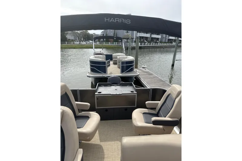 Slide: The Image of 2025 Harris Cruiser 230 pontoon boat with comfortable seating, docked by a serene waterfront. - 5