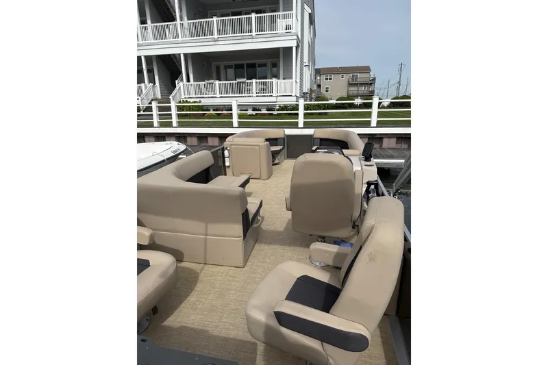 Slide: The Image of 2025 Harris Cruiser 230 pontoon boat with beige seating, docked near waterfront homes. - 6