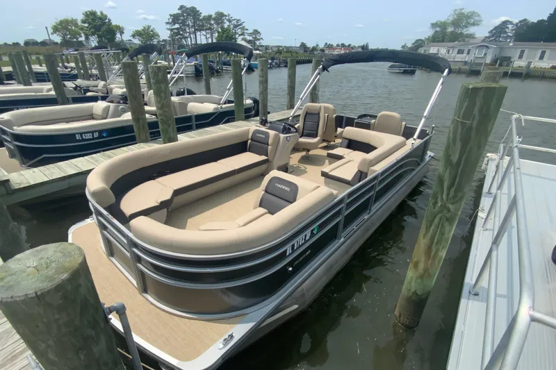 The Image of 2025 Harris Cruiser 230 pontoon boat docked at a marina, featuring spacious seating. - 1