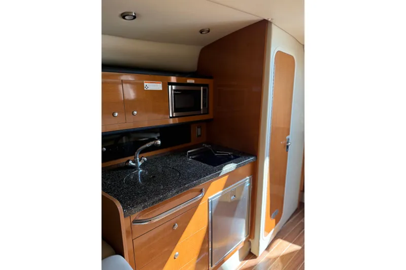 Slide: The Image of 2009 Chaparral 290 Signature yacht interior with kitchenette, featuring wood cabinetry and modern appliances. - 13