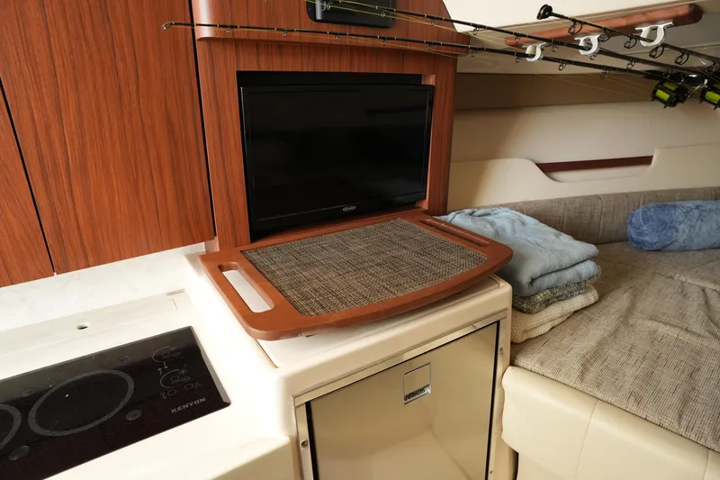 Slide: The Image of 2024 Grady-White Express 330 cabin interior with TV, kitchenette, and fishing rods. - 63
