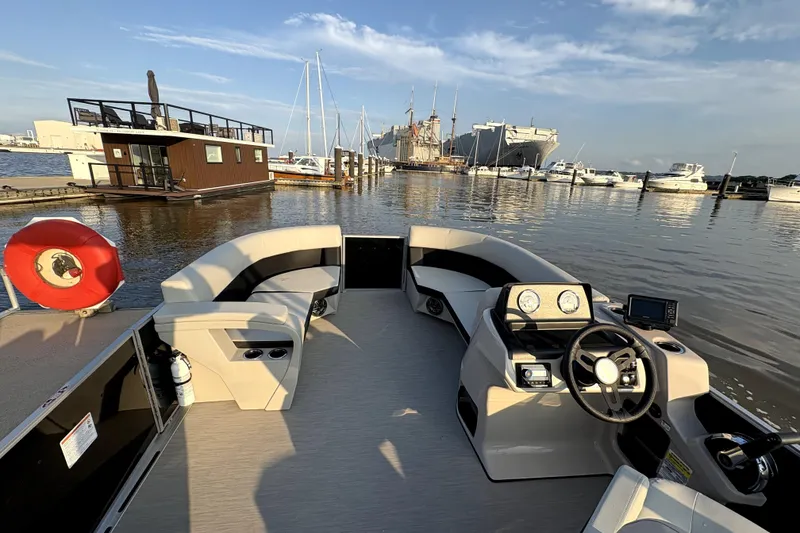 Slide: The Image of 2025 Harris Breeze 230 pontoon boat interior at marina, featuring modern seating and steering console. - 3