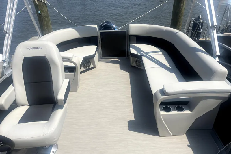 Slide: The Image of 2025 Harris Breeze 230 boat interior with plush seating and cup holders, docked by the water. - 7