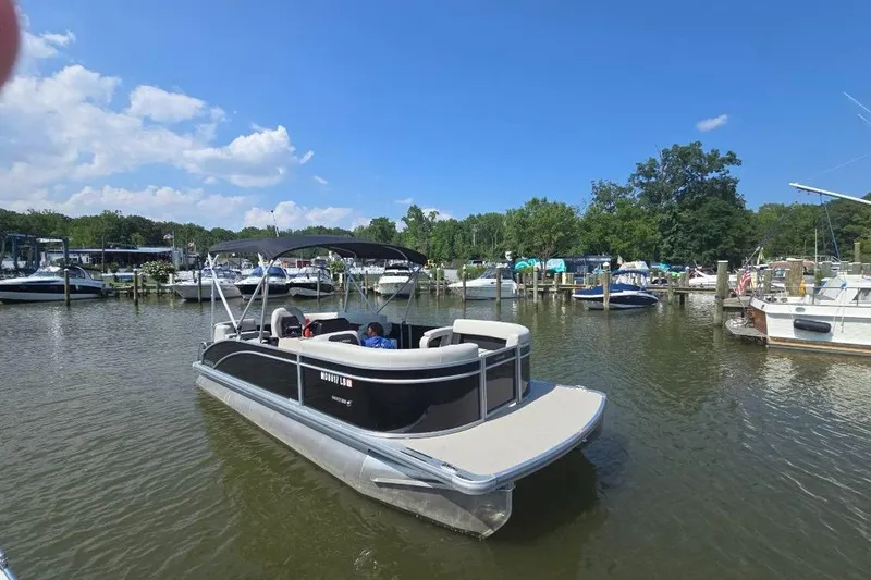 Slide: The Image of 2025 Harris Breeze 230 pontoon boat docked in a scenic marina under a clear blue sky. - 4