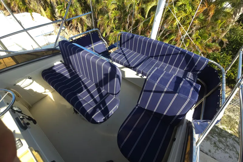 Slide: The Image of 2004 Legacy Yachts Sedan Flybridge with striped seating, surrounded by lush greenery. - 21