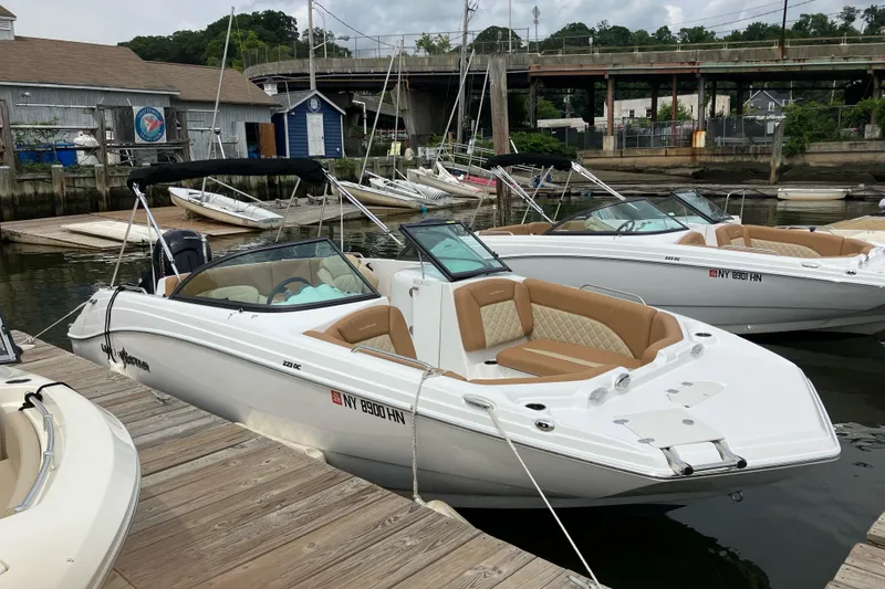 The Image of 2025 NauticStar 223 DC Deck boat docked at a marina with tan seating. - 1