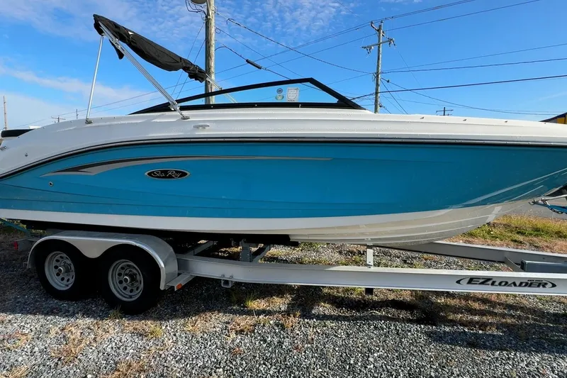The Image of 2024 Sea Ray SPX 230 boat on trailer, blue and white design, sunny day. - 0