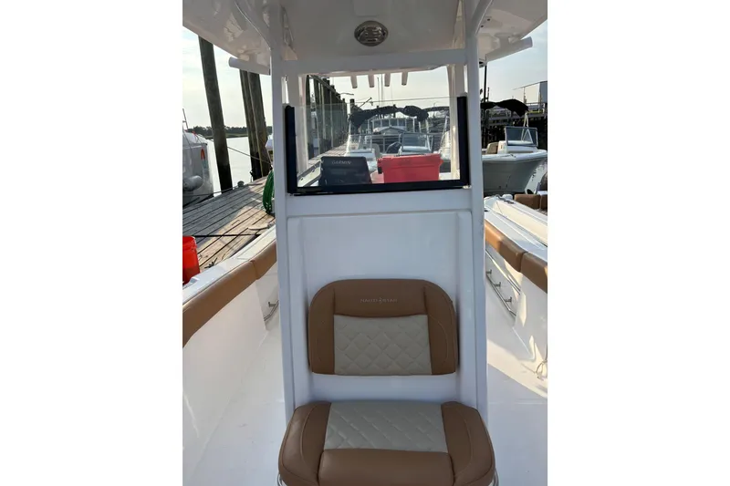 Slide: The Image of 2025 NauticStar 242L Offshore boat interior with tan seating and dock view. - 8