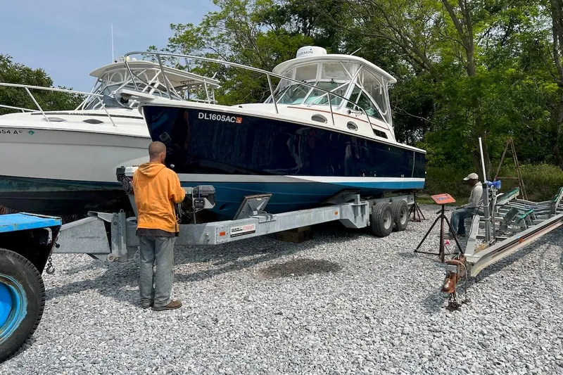 Slide: The Image of 2006 Back Cove 26 boat on trailer, two people nearby, surrounded by trees and gravel. - 11