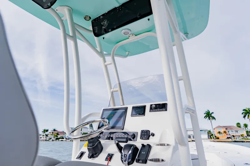 Slide: The Image of 2024 Key West 250 Bay Reef boat console with steering wheel and controls, against a coastal backdrop. - 25