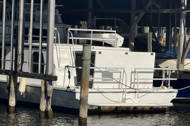 Slide: The Image of 1999 Gibson Houseboat 50 docked in a marina, partially sheltered by wooden structures. - 4