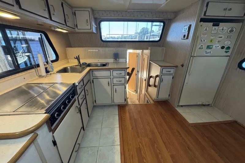 Slide: The Image of 1999 Gibson Houseboat 50 kitchen with white cabinets, stove, sink, and large windows. - 43