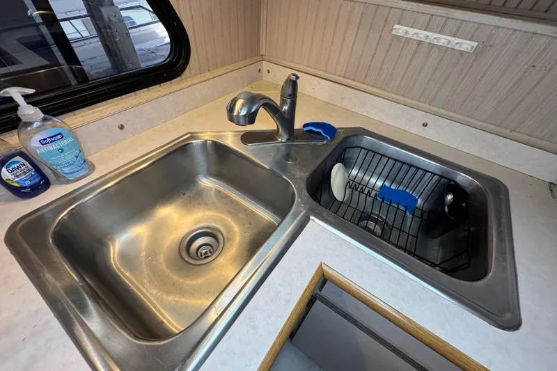 Slide: The Image of Kitchen sink area on a 1999 Gibson Houseboat 50, featuring dual basins and cleaning supplies. - 44