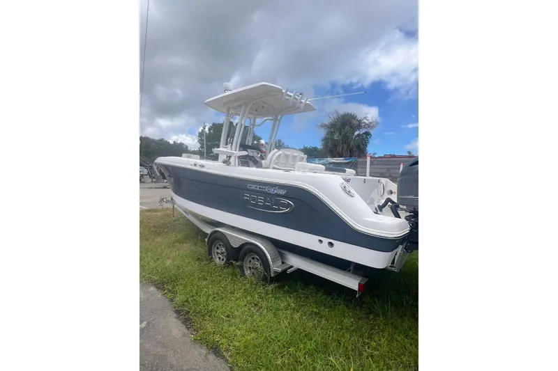 The Image of 2021 Robalo R242 Center Console boat on trailer, parked on grass under cloudy sky. - 0