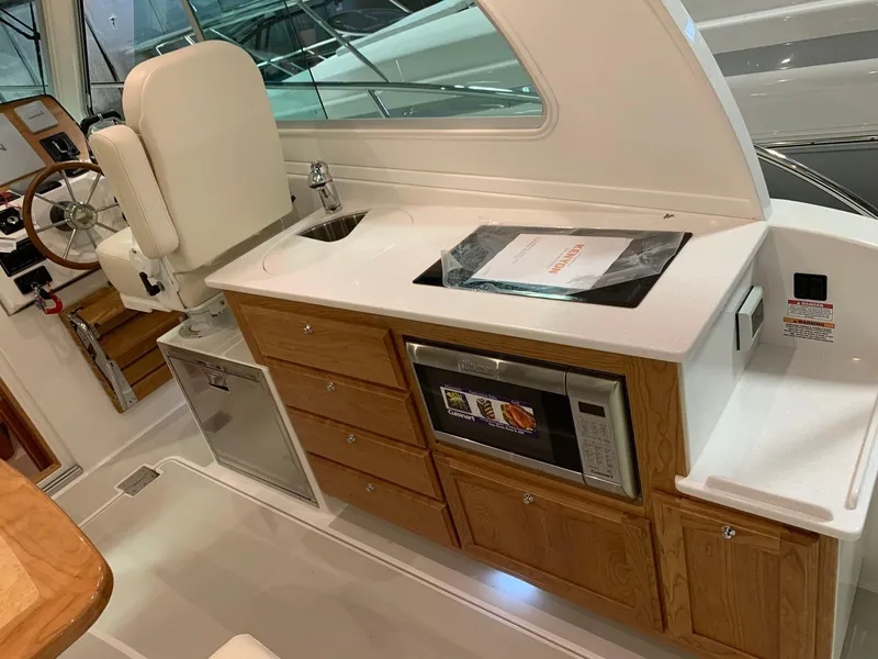 Slide: The Image of 2027 Back Cove 34O Hardtop Express interior with kitchenette, featuring sink, microwave, and wooden cabinetry. - 5