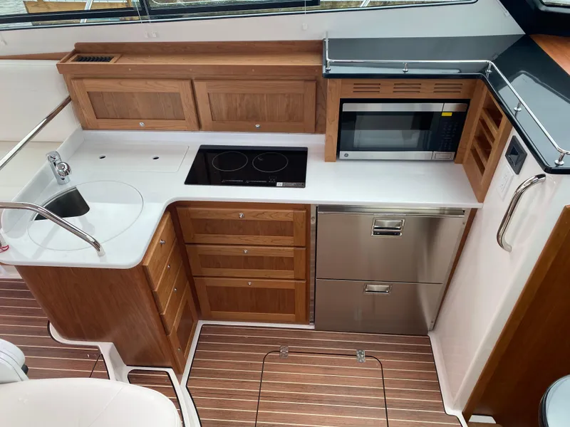 Slide: The Image of 2025 Back Cove 37 Hardtop Express kitchen with wood cabinetry, stove, microwave, and stainless steel appliances. - 12