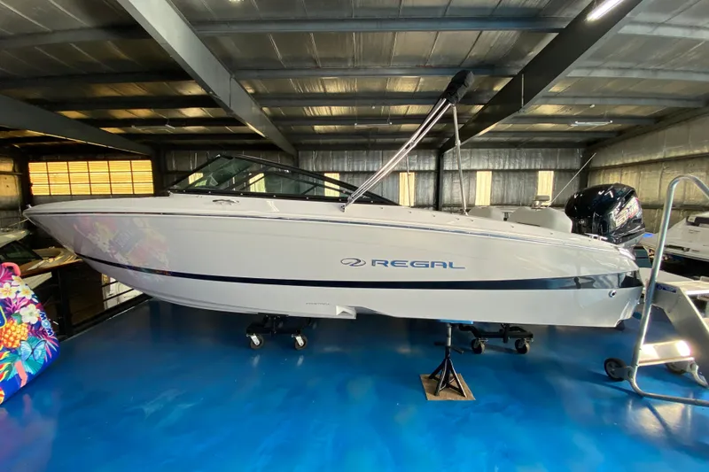 Slide: The Image of 2025 Regal LX2 boat in showroom, sleek design, metallic finish, indoor display. - 2