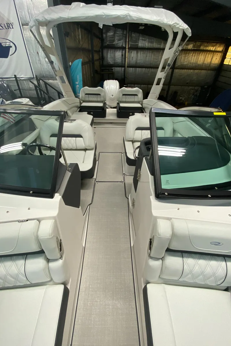 Slide: The Image of 2025 Regal LX6 boat interior with white seating and dual windshields in a showroom. - 14